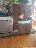 Photo showing two large Technics stereo speakers, one complete with speaker cones, one gutted. Small white mini fridge with paint peeling visible. Apple Macintosh desktop computer tower in front.