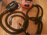 Orange Cage Master Plus and black Blaster dryers with hoses laid out on wood floor