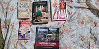 Six books laid out on floral fabric background including Nora Roberts, Tori Spelling titles, motorcycle book and vampire-themed book