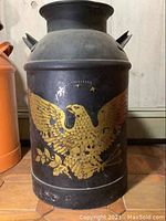 Black milk jug painted with eagle decal, showing wear and missing top