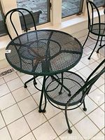 Full view of the metal cafe table and one chair showing the mesh tabletop and chair seat and overall construction.