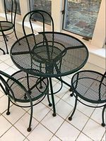 Full view of the green metal round mesh cafe table with three matching chairs.