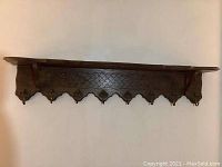 Full view of the carved wooden wall shelf showcasing its length, depth, and the row of brass hooks underneath.