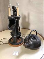 Cast iron water pump lamp with two electric candle bulbs and cast iron steam kettle on round table.