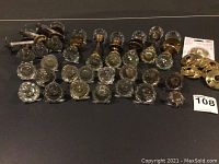 Full lot display of over 25 vintage glass door knobs with metal backplates laid out in rows.