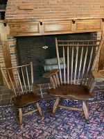 Pair of wooden rocking chairs set before a brick fireplace on a patterned rug.