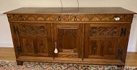 Front view of carved oak sideboard showing two drawers and three doors closed