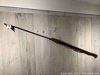 Full-length view of harpoon mounted horizontally against light wood panel