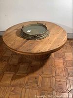 Overview of round wooden spool coffee table with brass porthole centerpiece