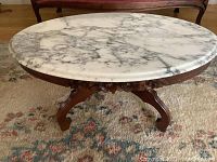 Full front view of oval marble topped coffee table with carved wooden base