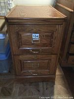 Front view of the oak filing cabinet with two drawers. Visible wood grain with metal handles and label holders.