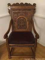 Full front view of one carved oak armchair showing carved back, arms, legs and leather seat cushion