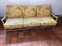 Front view of vintage rattan 3-seater couch with floral cushions, showing the wooden frame and fabric cushions with floral pattern.