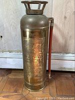 Full view of the vintage brass fire extinguisher, showing cylindrical shape, brass body, handle, and hose attachment.