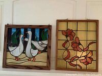 Both stained glass art pieces framed in wood, hanging side by side on a wall. The geese design is on the left, floral design on the right.