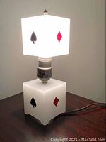 Front view of lamp with the spade and diamond suits visible on the shade and base, turned on with bright white light.