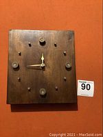 Front view of the square wooden clock with bullet shell casings used as hour markers on a dark stained wood block with brass clock hands.