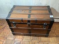 Full view of closed wooden trunk showing top and front with metal bands and lock.