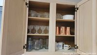 Cabinet with various mugs on two shelves; clear glass beer mugs on bottom left, copper mugs top right, ceramic mugs bottom right, and several clear drinking glasses.