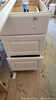 Photo showing white kitchen base cabinet with three paneled drawers, without countertop, with a water bottle placed on top for scale.
