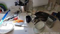 Overview of kitchen items including mixing bowls, pans, mugs and utensils on counter.