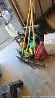 Full view of the garden tools and accessories grouped together in garage showing rakes, sprayer, leaf blower, and gas can.