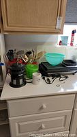 Photo of kitchen counter with various kitchen items including T-fal electric grill, bowls, grater, colander, coffee mug, French press, and utensils.