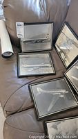 View of four framed black and white photos of classic commercial airplanes on brown leather surface.