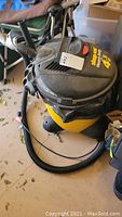 Full view of Shop Vac showing yellow and black body, motor housing with handle and hose.