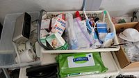 Photo showing a basket with medical supplies, a white hairdryer, electric toothbrush charger, green alcohol wipes, and other assorted small household items.