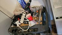Black and red electric drill, white power bar extension cord, adjustable wrench, and other assorted tools and hardware on a black rolling tool cart.