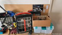 Photo of tool organizer with multiple compartments alongside a clear plastic storage box and cardboard box with small tools and parts.