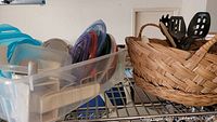 Plastic containers with colorful lids and a woven basket with black kitchen utensils