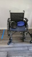 Front view of black wheelchair with blue neck pillow and black brace on seat