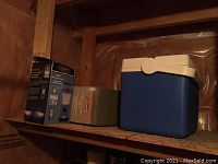 Photo shows blue portable cooler, a cardboard box with lantern, and another box on a wooden shelf