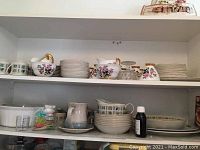 Two shelves with two sets of dishes including floral pattern plates, bowls, creamers, sugar bowls with gold handles, and serving pieces