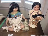 Photo showing both Indigenous dolls sitting and standing by window next to a small fur-like animal figure.