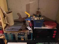 Photo showing 12" dovetail jig box, blue container with hardware, beige door handle, and DeLonghi toaster oven on right side