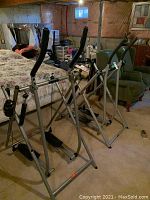 Two Tony Little Gazelle Edge steppers side by side in basement setting showing full frame, pedals, and handles, one with speed meter missing