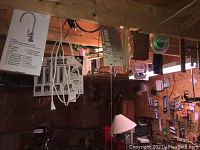 Work lamp with orange extension cord and assorted hardware boxes hanging from wooden rafters in workshop area.