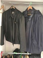 Two leather jackets hanging on hangers in a closet, one black and one navy blue.