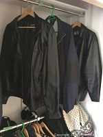 Two black leather jackets and one blue nylon windbreaker hanging on hangers in a closet.