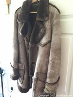 Brown sheepskin coat hanging showing front and lapel details with fur trim on collar, pockets, and cuffs