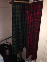 Two wool plaid kilts hanging side by side, one green-blue plaid and one red-green plaid.