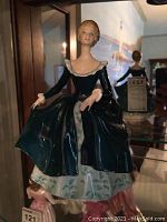 Front view of the Royal Doulton Janine HN2461 figurine, showing the woman in a dark teal dress with floral underskirt.