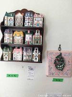 Full view of the 12 spice jars arranged on the dark wooden wall-mounted rack with the metal leaf wall plaque on the right on pink floral background.