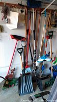 Photo showing shovels, rakes, brooms, Swiffer mop, and yard decor leaning against a garage wall.