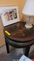 Round wooden table top with decorative inlay and part of lamp and framed art showing on top.