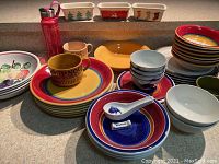 Photo showing colorful ceramic Furio plates and bowls with concentric circle designs in yellow, red, and blue, along with Asian soup bowls with matching ceramic spoons and other assorted bowls and a Starbucks water bottle.