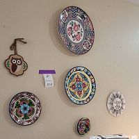 Overview of the wall showing the six decorative plates, sun face wall ornament, and wooden owl wall hanging